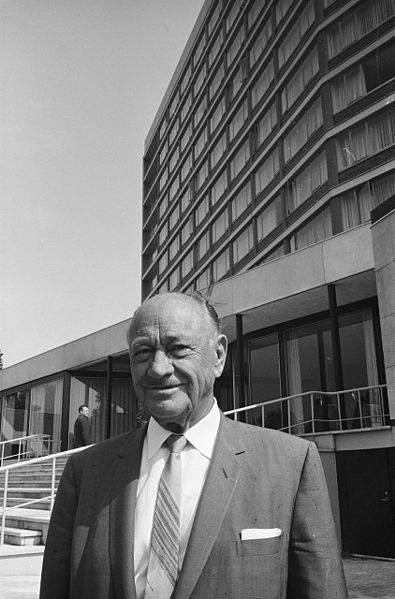 black and white picture of Conrad Nicholson Hilton, in the background you can see his hotel in Amsterdam.
