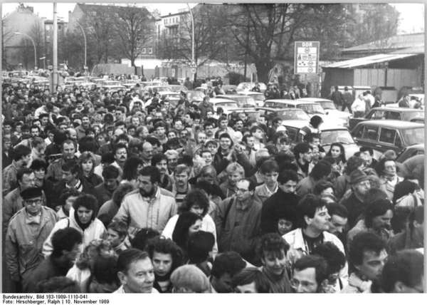 Black-and-white photograph of a mass of people (including cars) that clusters at the border crossing Invalidenstrasse in Berlin on 10 November 1989.