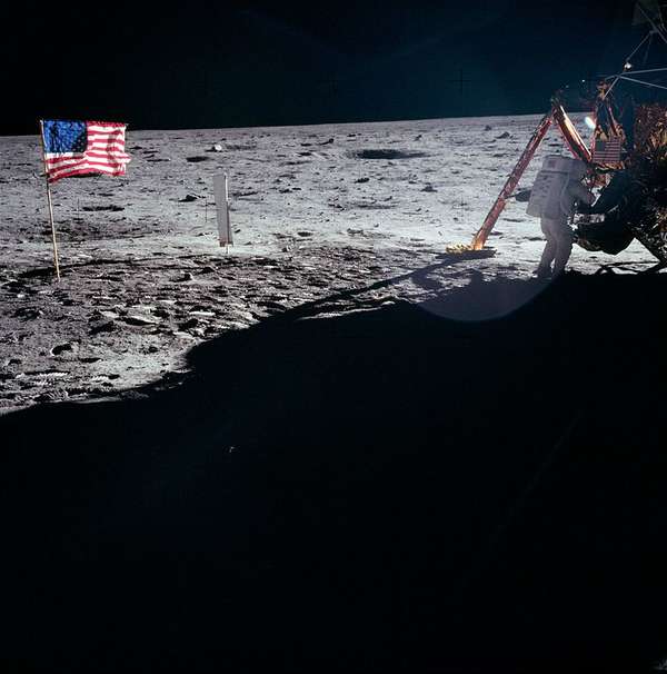Picture of Neil Armstrong working on the moon near lunar module Eagle, on the left side of the picture you can see the American flag.